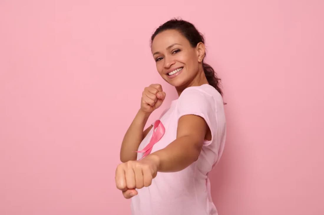 Mujer con camiseta y lazo rosado en posición de lucha, medicina prepagada contra el cáncer
