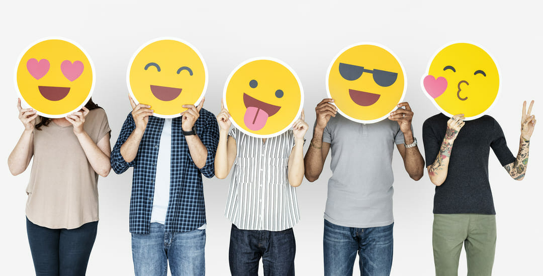Personas cubriendo sus rostros con emojis felices por el Día del Comportamiento Humano