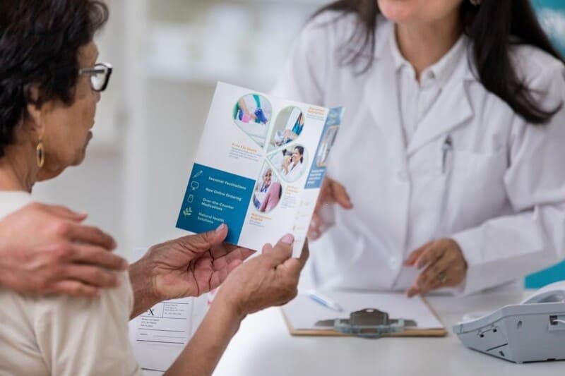 Médica mostrando un folleto a una paciente mayor, beneficios únicos del seguro de salud